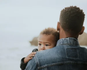 a young dad holding his infant son who looks over his fathers shoulder