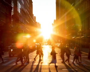 looking down a busy city street at sunset with many people crossing in a crosswalk