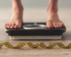 a pair of feet on a scale with a measuring tape in the foreground