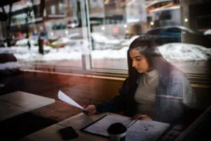 A woman sitting in a coffee shop reviewing papers in a binder