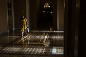 a woman in a yellow dress walking in the foyer of a building with a chandelier in the background