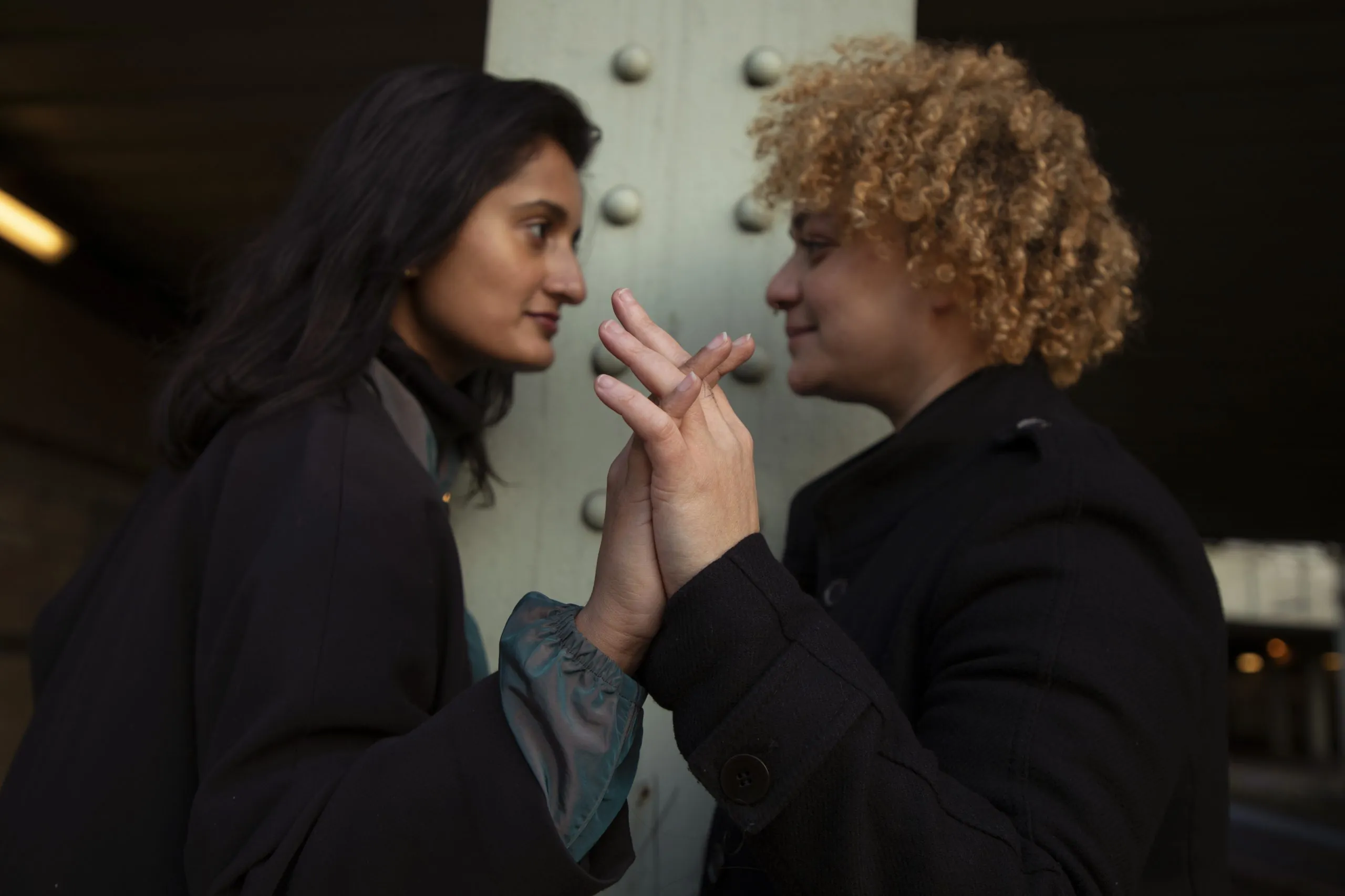 two woman facing each other clasping a single hand with each other