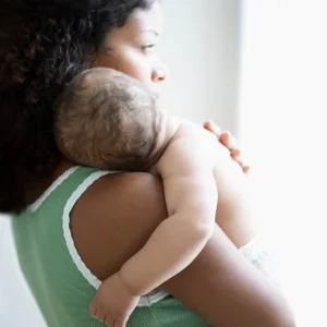 A woman holding a baby over her shoulder with her hand on his back.