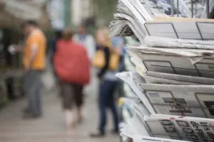 Newspaper rack on street, blurred people walk in the background