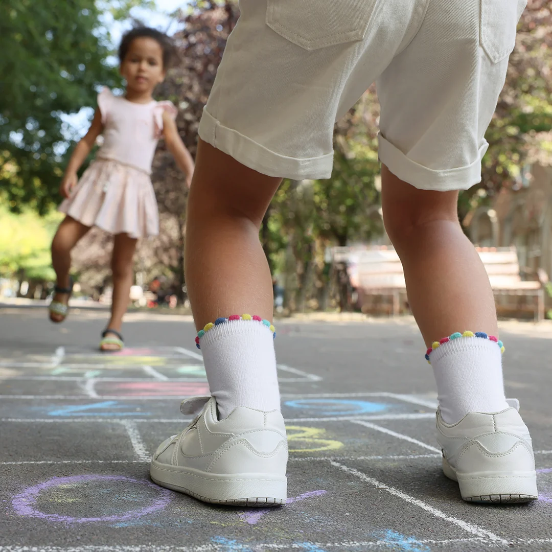 Children's feet wearing white sneakers playing hopscotch on a playground